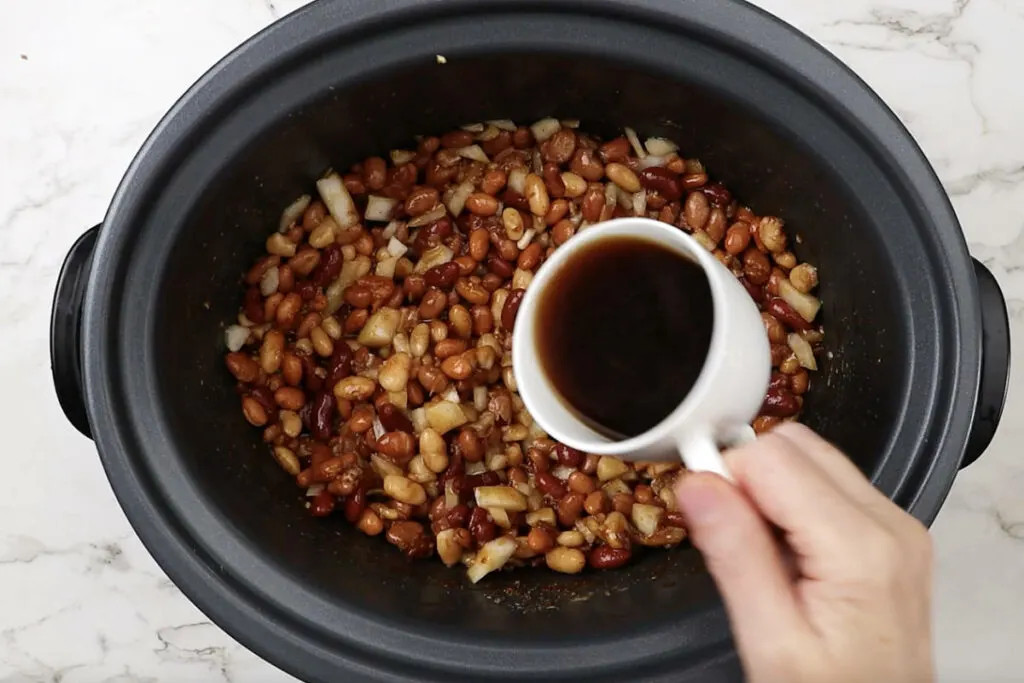 Adding coffee to a crockpot with beans.