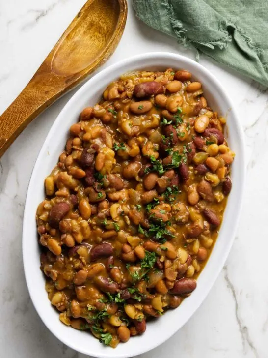 A dish with slow cooker baked beans next to a spoon.