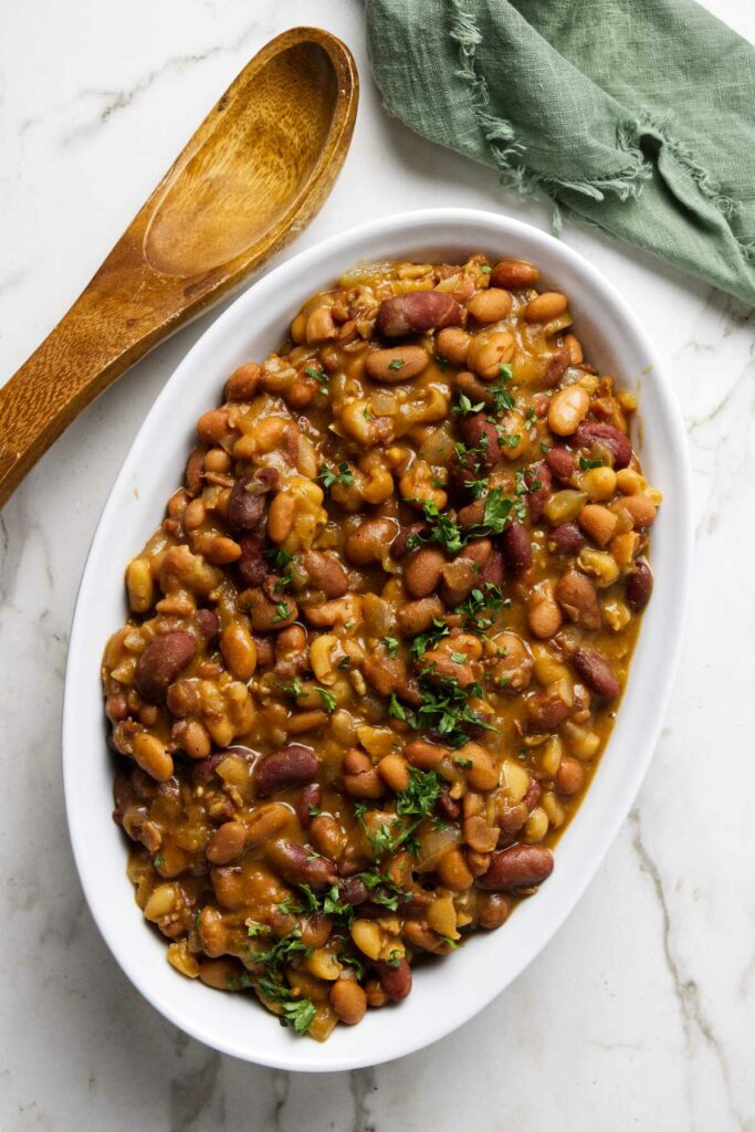 A dish with slow cooker baked beans next to a spoon.