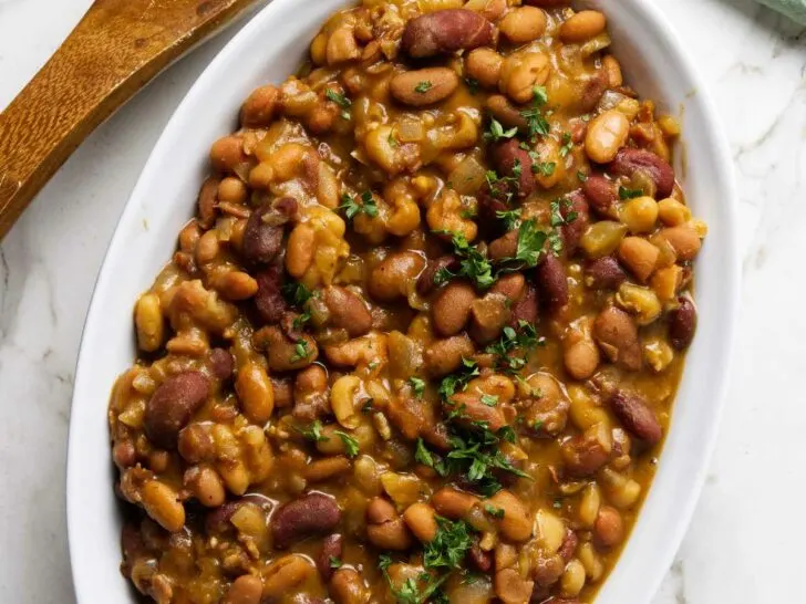 A dish with slow cooker baked beans next to a spoon.