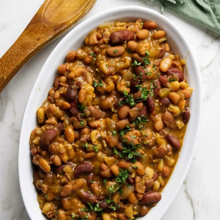 A dish with slow cooker baked beans next to a spoon.