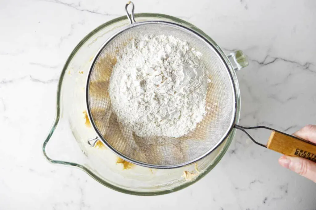 Sifting flour into the mixing bowl to make a sugar cookie recipe for Christmas cutouts.