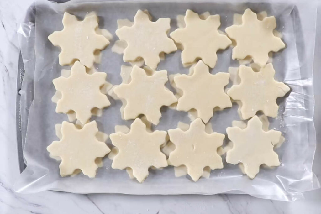 Stacking raw sugar cookies on a baking sheet to freeze before baking.