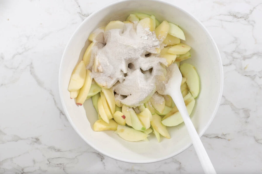 Mixing sugar, flour, cornstarch, and spices with the apple slices.