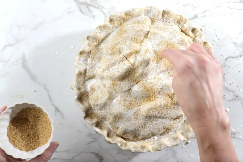 Sprinkling sugar on top of the deep dish apple pie.