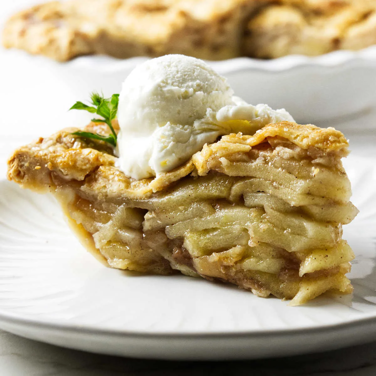 A double crust deep dish apple pie slice on a plate with ice cream.