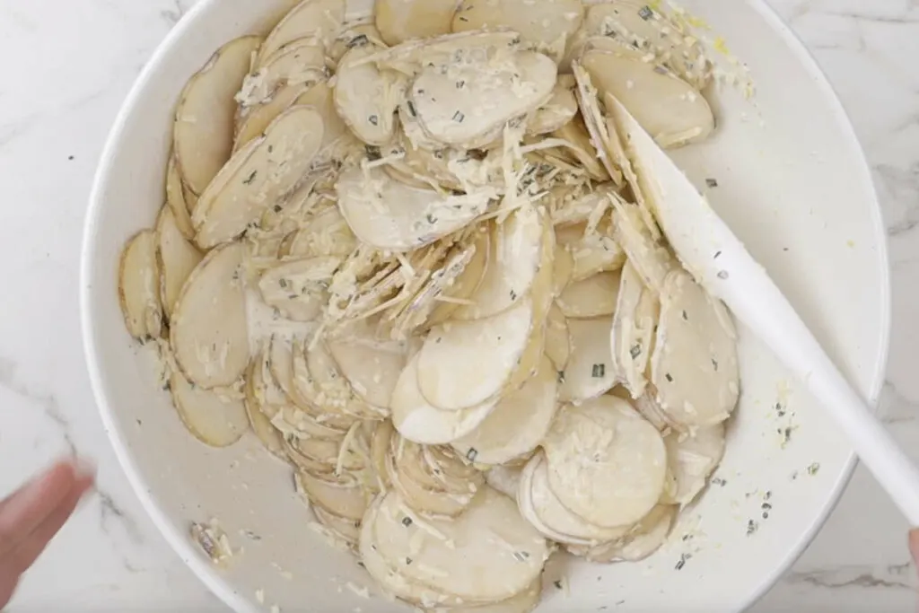 Coating slices of potatoes in the cream and cheese mixture.