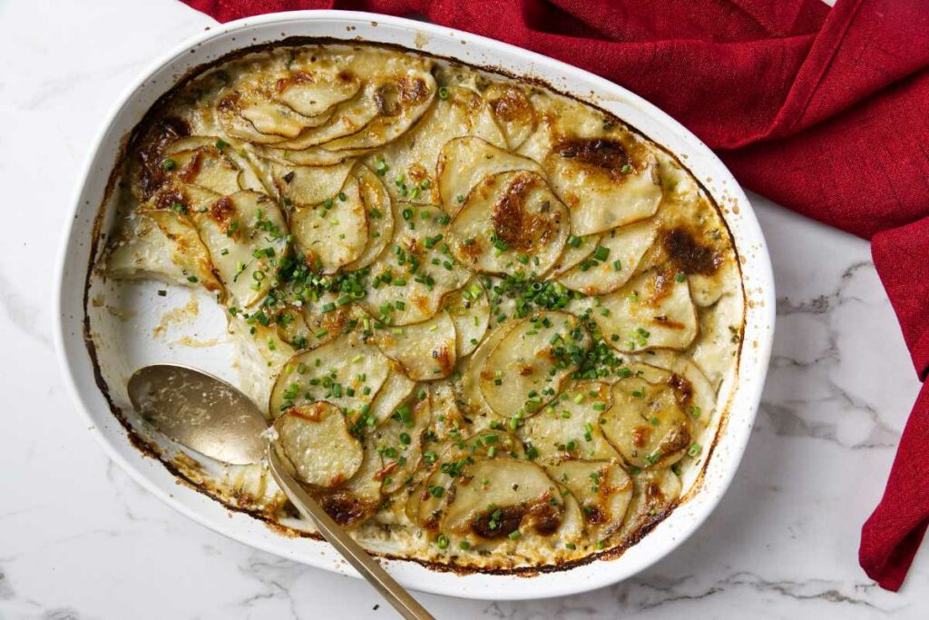 A spoon scooping out scalloped potato gratin from a casserole dish.