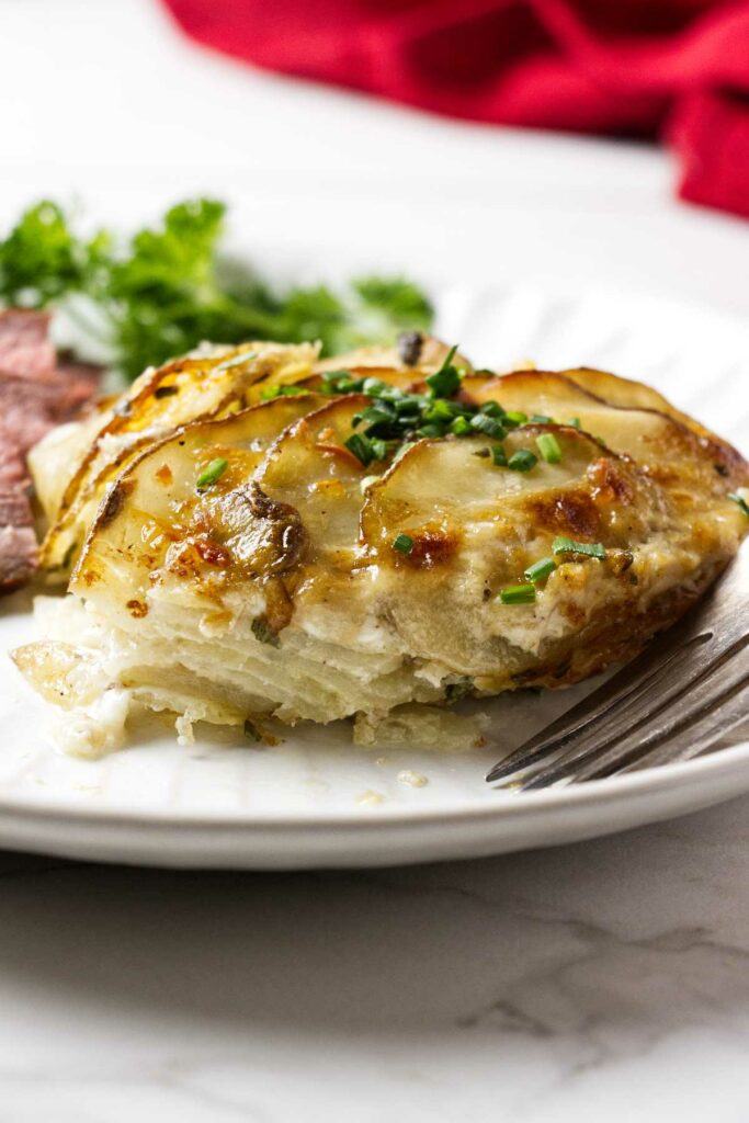 A serving of cheesy gratin potatoes on a plate with steak and salad.