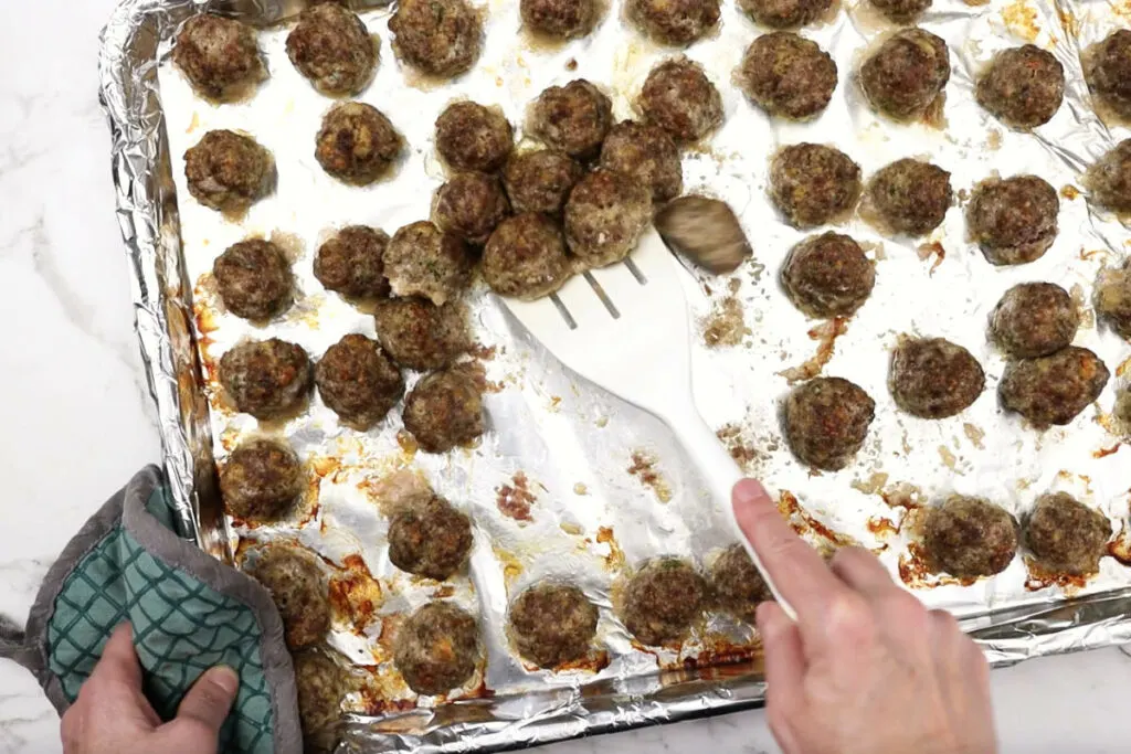 Transferring cooked meatballs to a different pan.