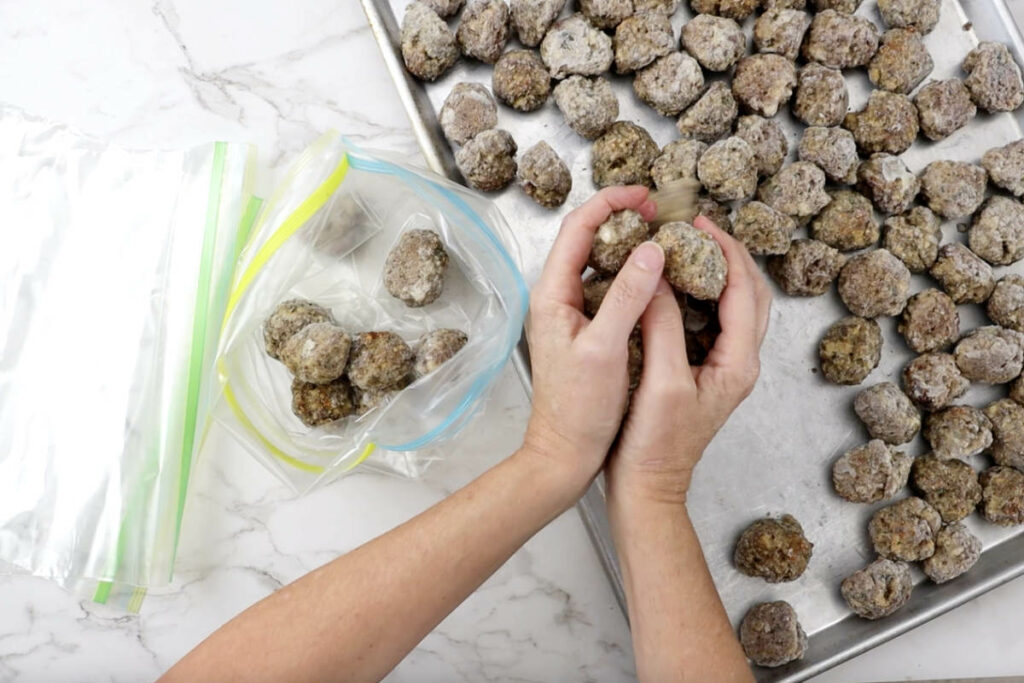 Transferring cooked frozen meatballs to freezer bags.