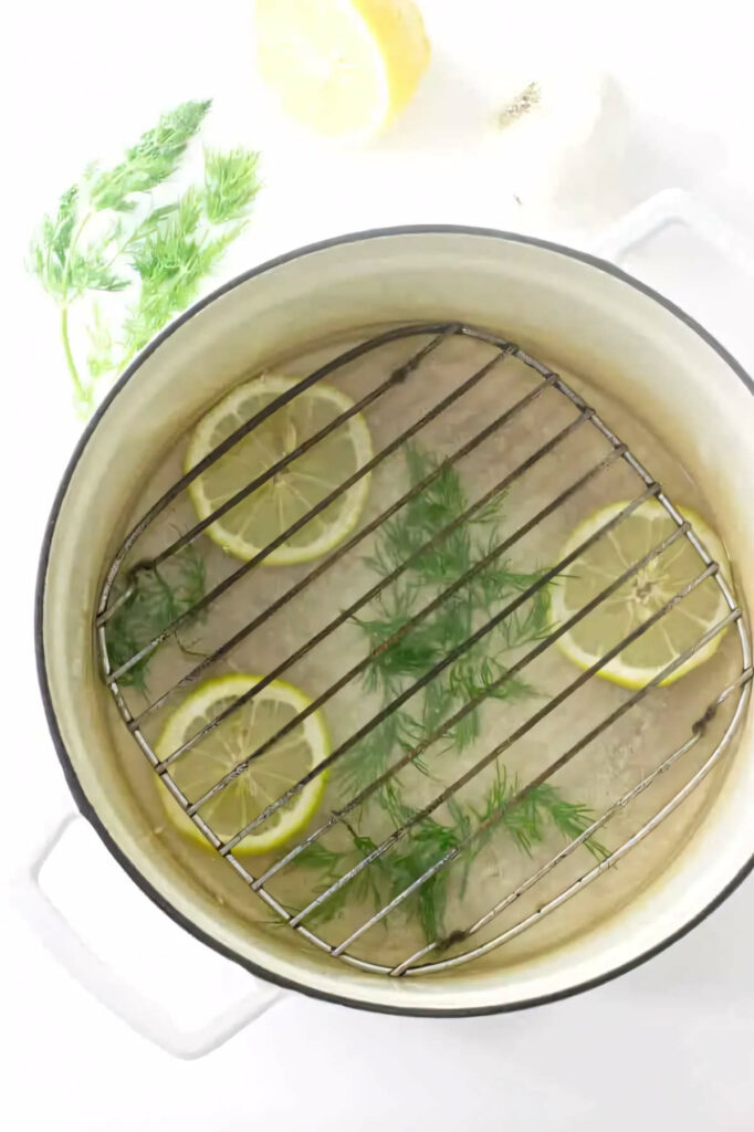 A pot with a rack to elevate salmon above water, dill and lemon.