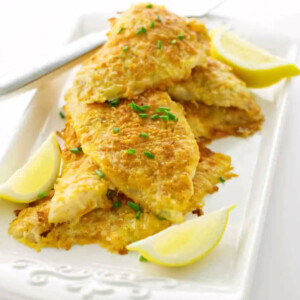 Baked parmesan sole fish on a serving platter with lemon wedges.