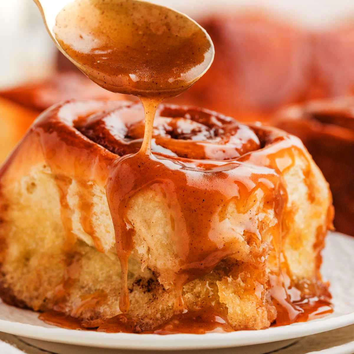 Drizzling caramel sauce over a sticky cinnamon roll.