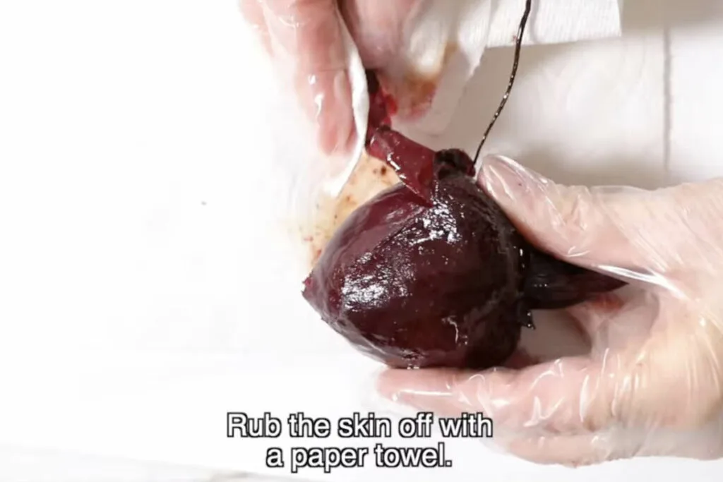 Using gloves and a paper towel to peel skin off a roasted beet.