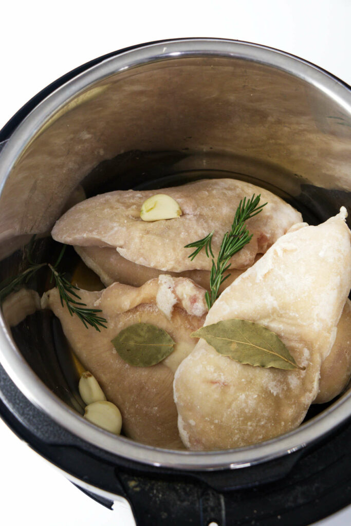 Several frozen chicken breasts in the instant pot with herbs.