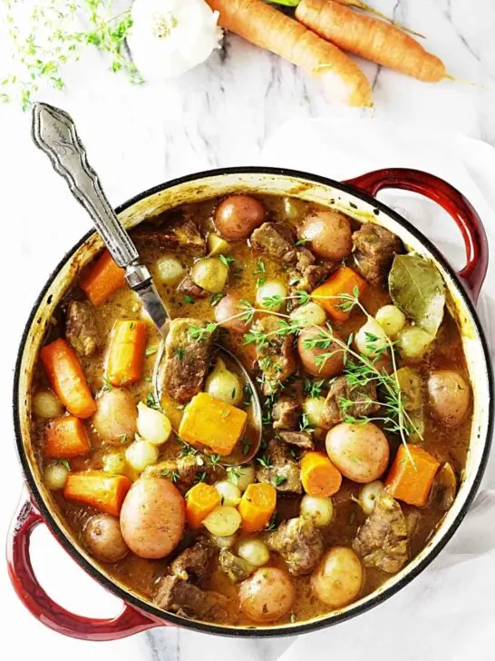 A large pot of lamb stew next to some veggies.