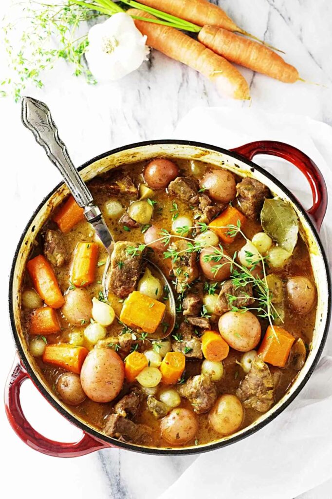 A large pot of lamb stew next to some veggies.