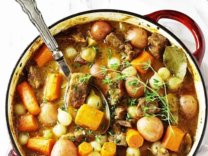 A large pot of lamb stew next to some veggies.