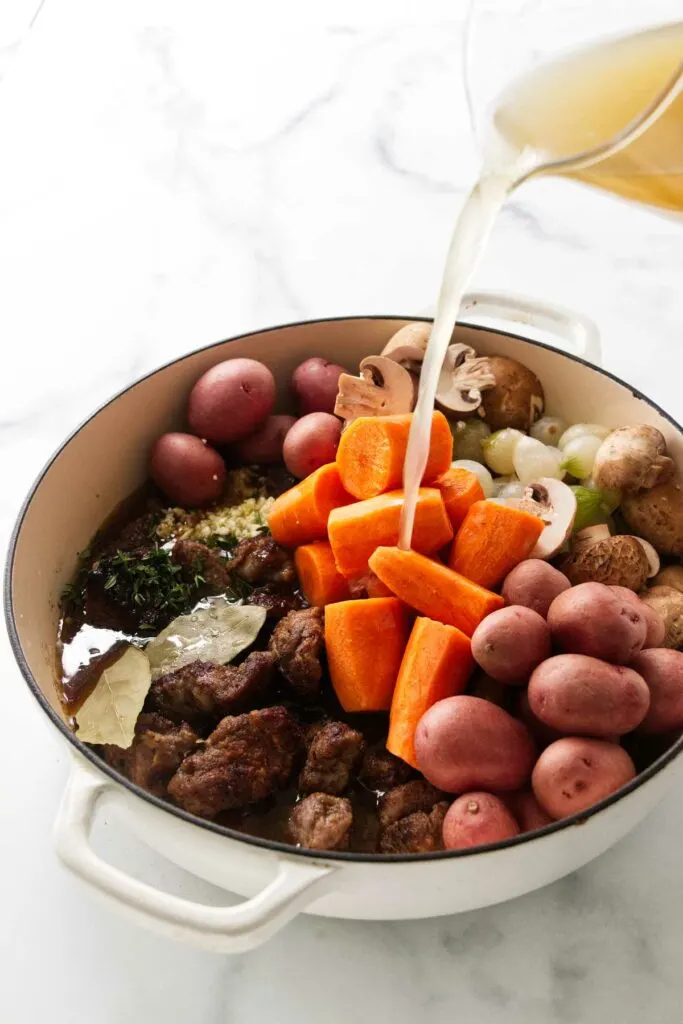 Adding chicken broth to the pot of stew with lamb.