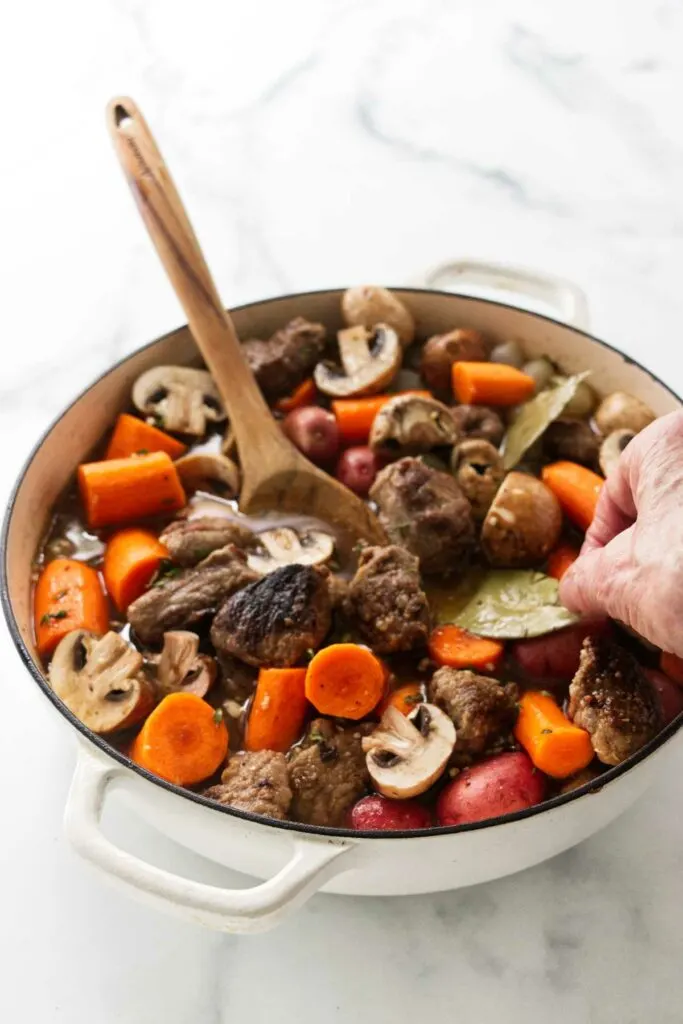 Adding herbs to the lamb stew in a Dutch oven.