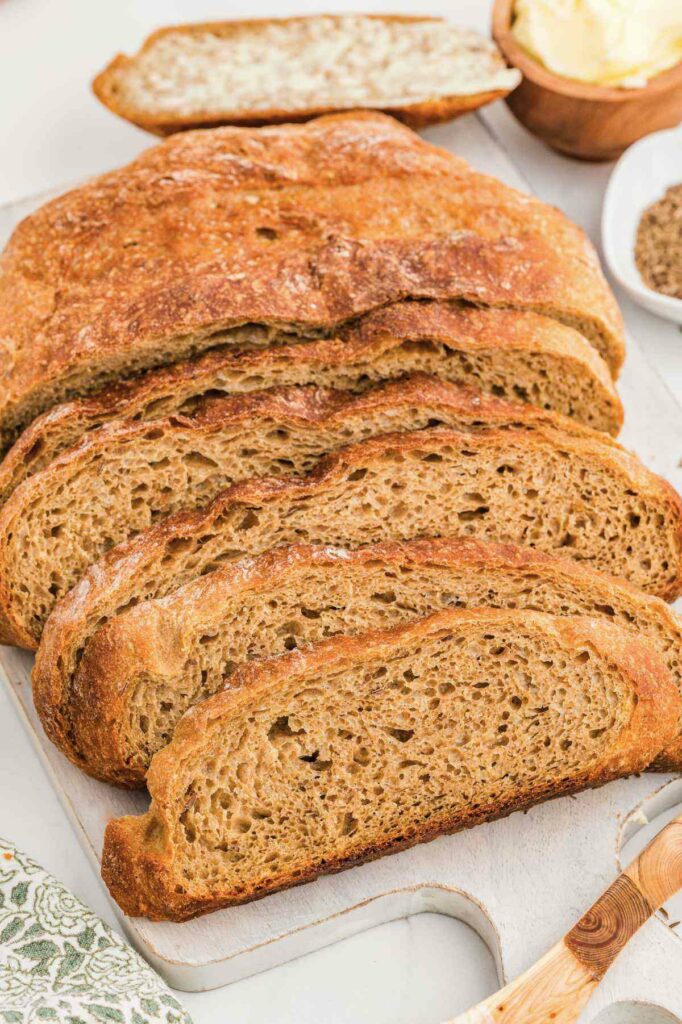 Slices of a simple rye bread recipe next to a dish of caraway seeds.