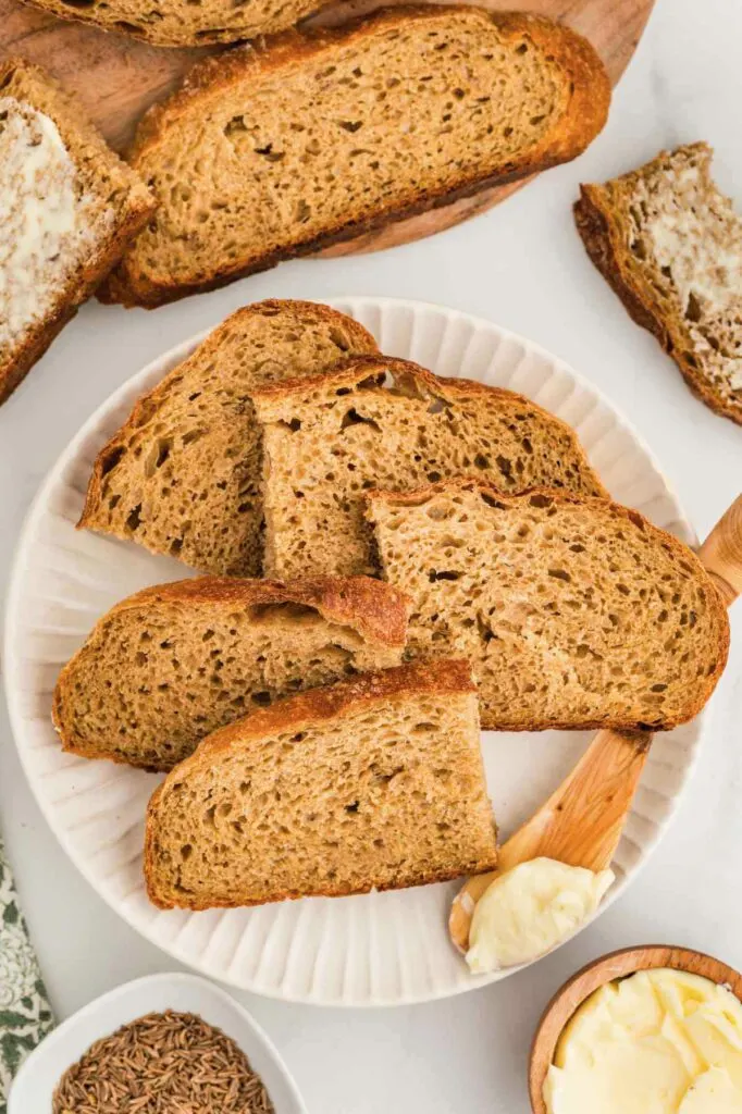 Slices of Dutch oven rye bread on a plate next to butter.