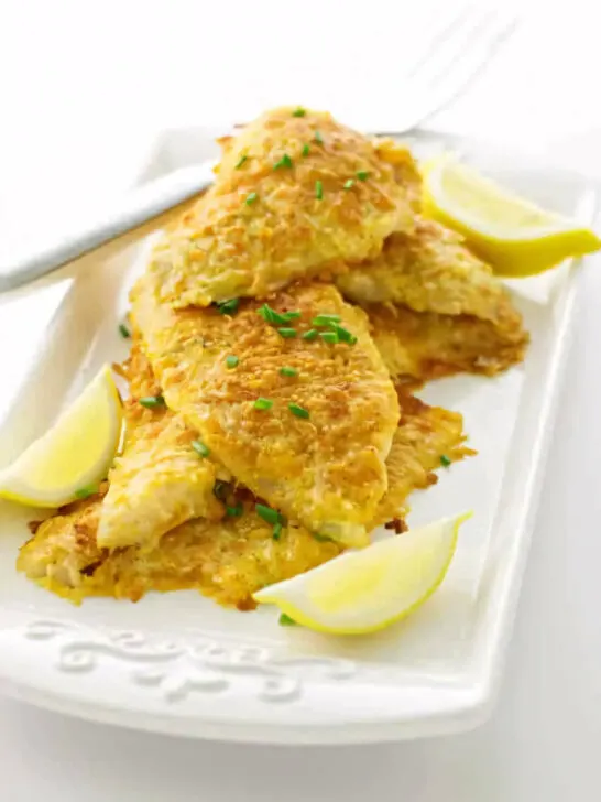 Several parmesan crusted sole fillets on a platter with lemon.