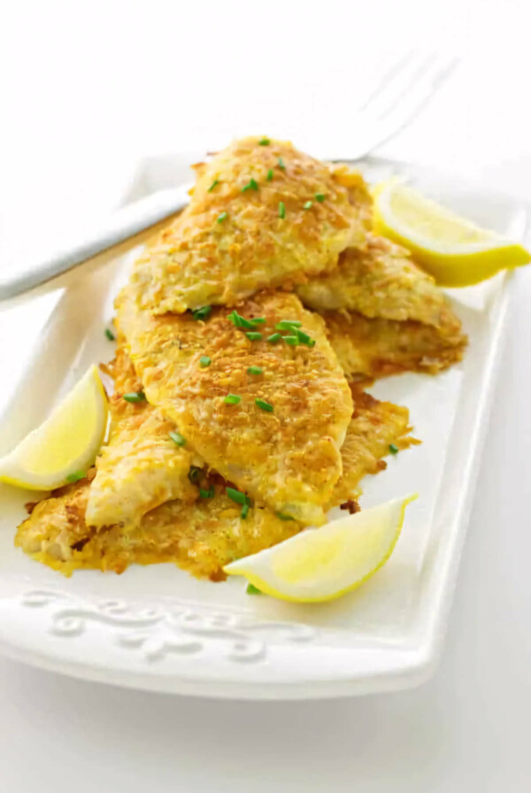 Several parmesan crusted sole fillets on a platter with lemon.