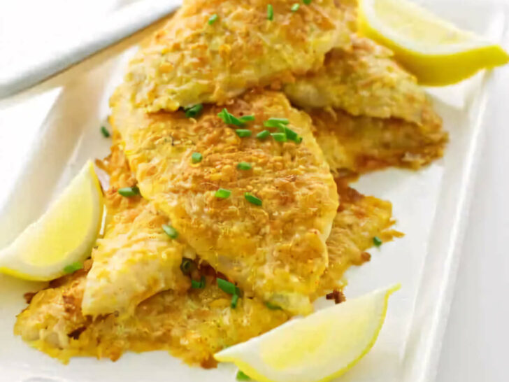 Several parmesan crusted sole fillets on a platter with lemon.