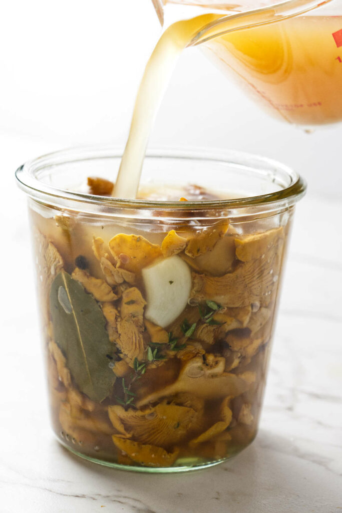 Pouring pickling brine over a jar of chanterelle mushrooms.