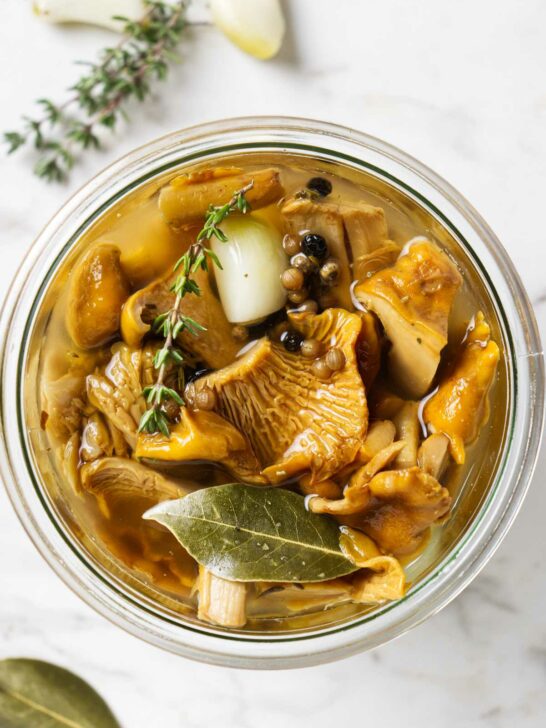 A jar of pickled chanterelles next to fresh thyme sprigs.