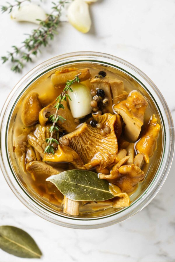 A jar of pickled chanterelles next to fresh thyme sprigs.