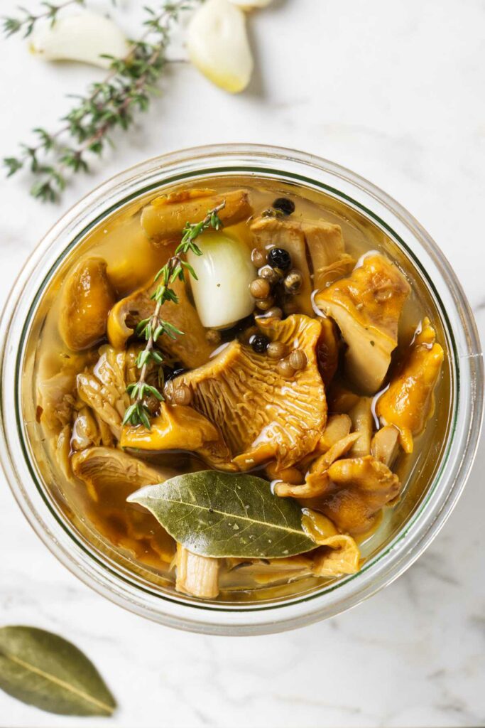 A jar of pickled chanterelles next to fresh thyme sprigs.