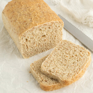 Slices of cracked wheat bread next to a loaf of bread and a knife.