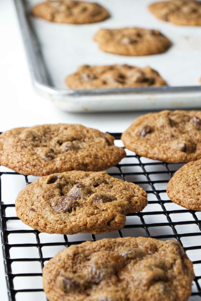 A batch of spelt chocolate chip cookies cooling on a wire rack.