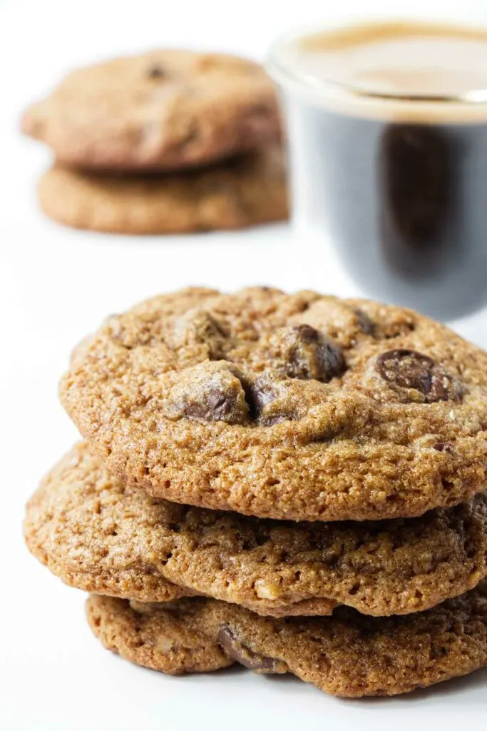 Three chocolate chip spelt flour cookies in front of a cup of coffee.