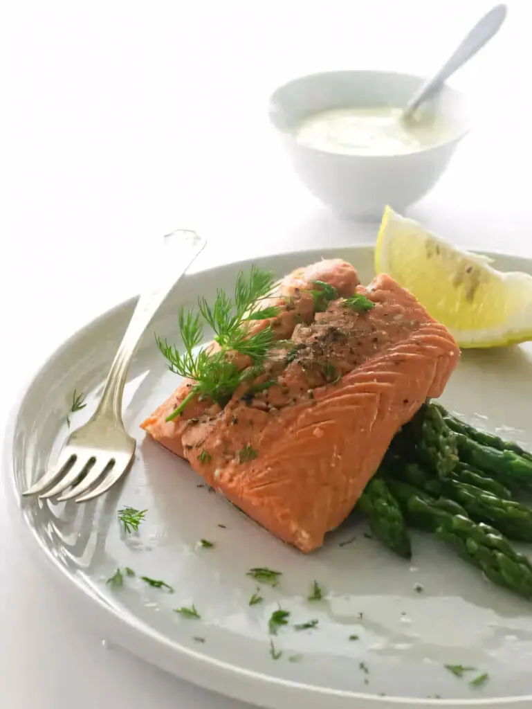 Steamed salmon on a plate with asparagus and a lemon wedge.