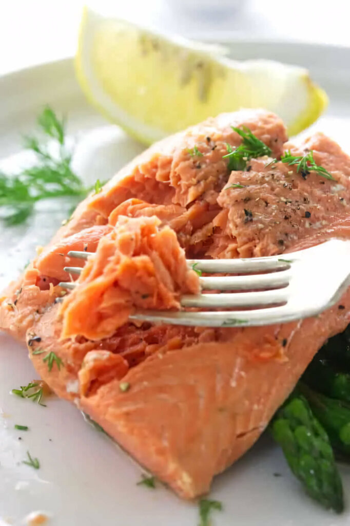 A fork flaking off some salmon cooked in a steamer.