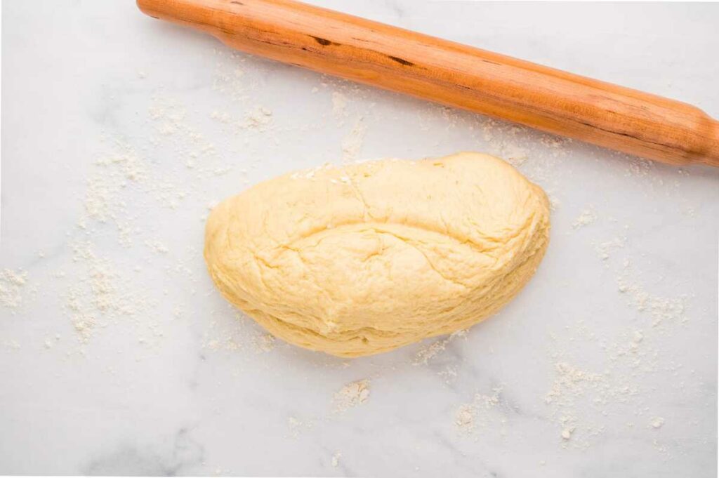 A rolling pin and cinnamon bun dough on a floured counter.