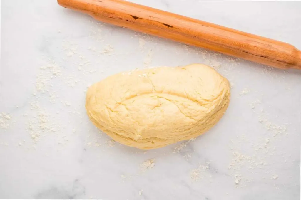 A rolling pin and cinnamon bun dough on a floured counter.