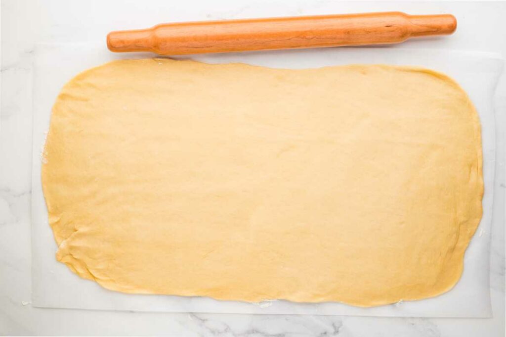 A rolling pin next to dough that is rolled out into a rectangle.