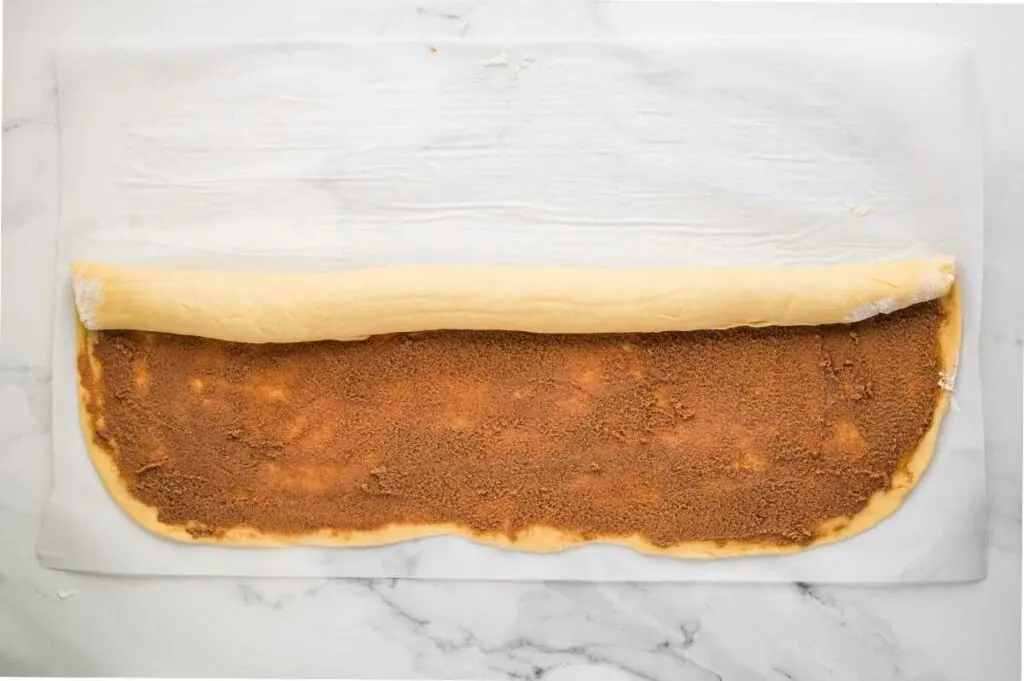 Dough spread with cinnamon-sugar filling, being rolled into a log.