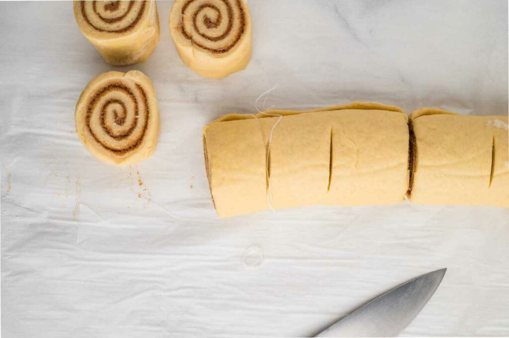 Rolled cinnamon roll dough filled with cinnamon-sugar, partially sliced into individual rolls, showing swirled layers of filling.