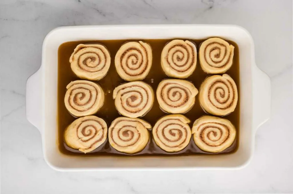 Unproofed cinnamon rolls arranged in a baking pan on top of a layer of sticky caramel sauce, ready to rise and bake.