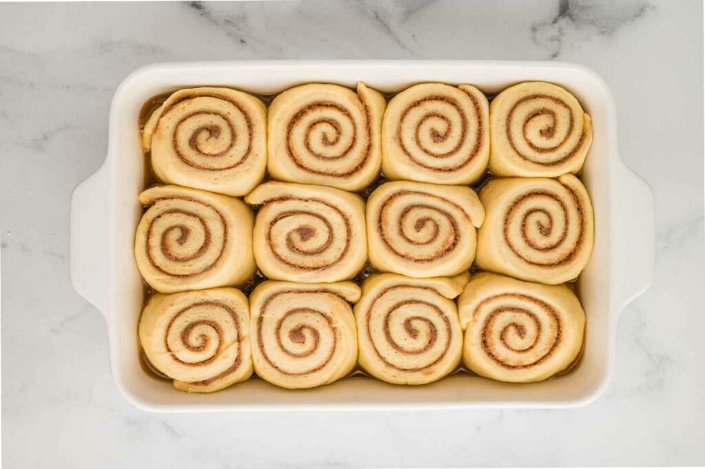 Proofed cinnamon rolls in a baking pan, nestled on a bed of sticky caramel sauce, now risen and ready for baking.