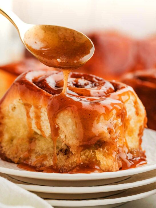 Sticky cinnamon rolls with gooey caramel sauce being dripped over the top.