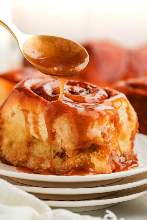 Sticky cinnamon rolls with gooey caramel sauce being dripped over the top.