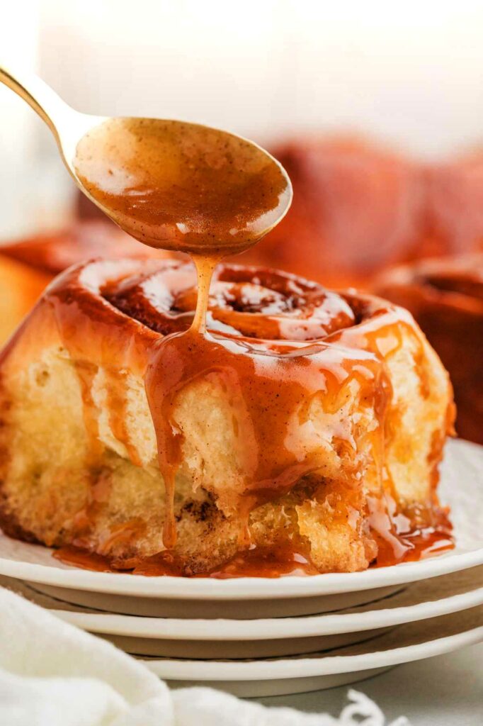 Sticky cinnamon rolls with gooey caramel sauce being dripped over the top.