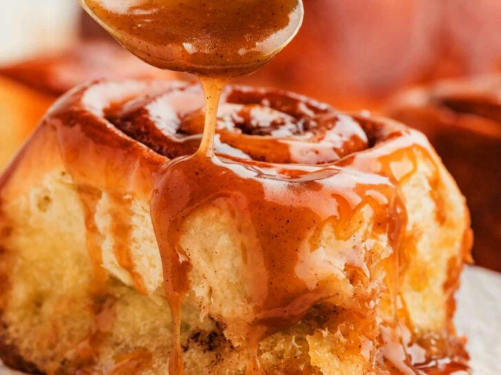 Sticky cinnamon rolls with gooey caramel sauce being dripped over the top.